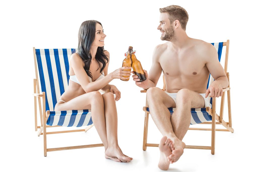 novio y novia tintineo con botellas de cerveza mientras se relaja en sillas de playa, aislado en blanco
   - Foto, imagen