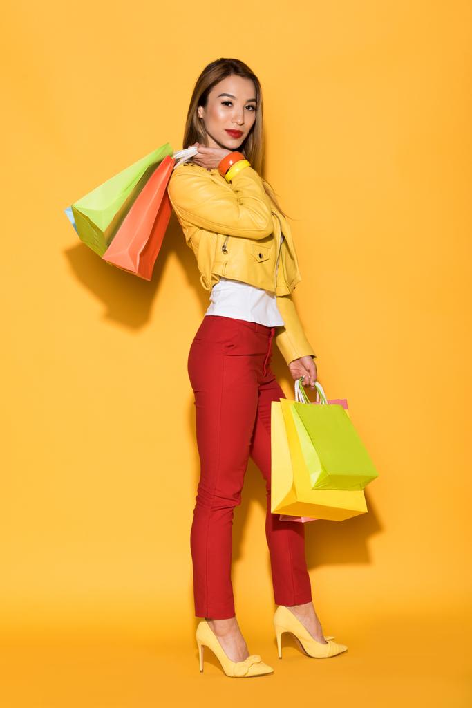asiática jovem mulher com sacos de compras no fundo amarelo
  - Foto, Imagem