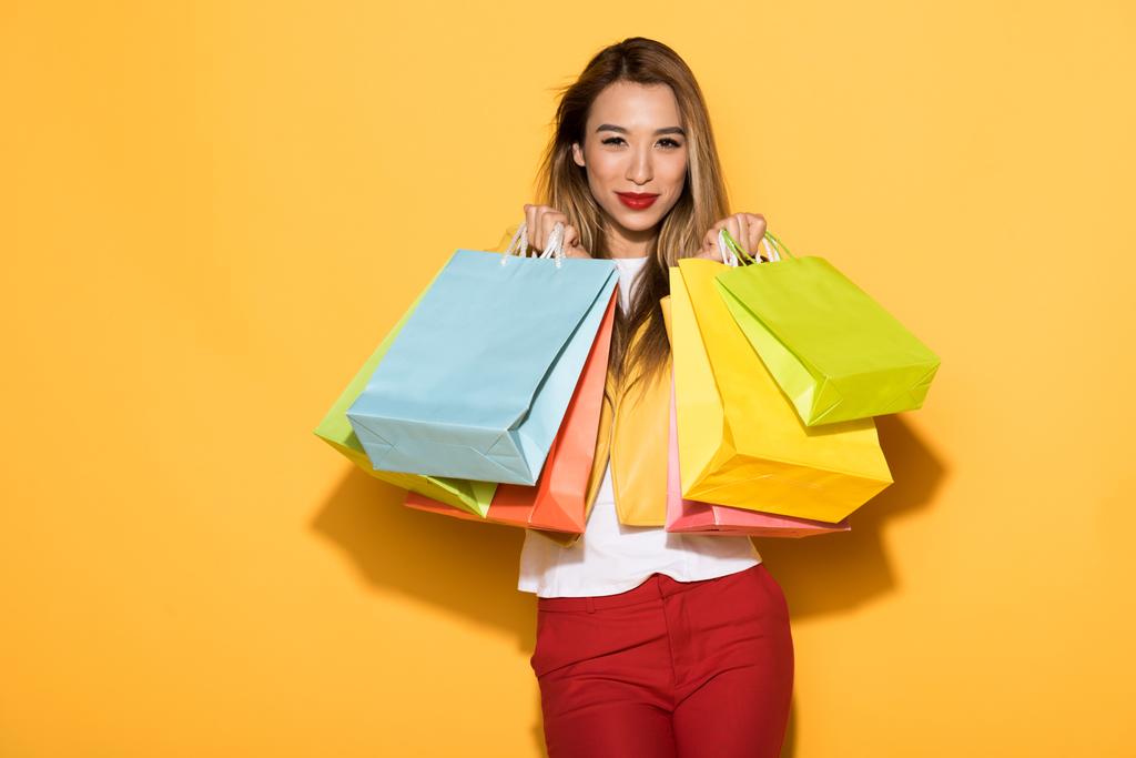 asiatische Shopperin mit Papiertüten auf gelbem Hintergrund  - Foto, Bild