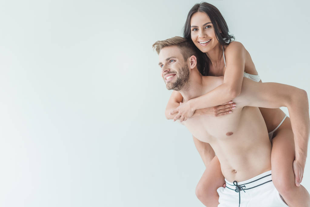 hermosa feliz pareja en traje de baño piggybacking aislado en blanco
 - Foto, imagen