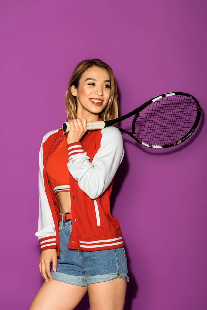 kaunis hymyilevä aasialainen tyttö tilalla tennis maila ja etsii pois eristetty violetti
  - Valokuva, kuva