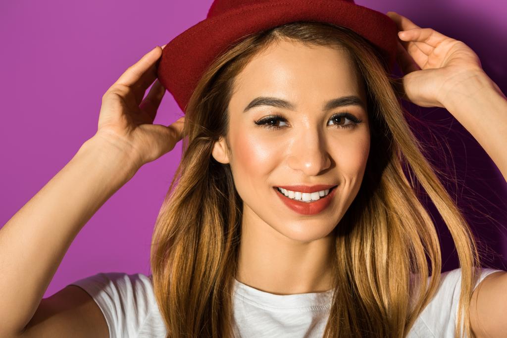 portrait en gros plan de belle jeune femme asiatique en chapeau souriant à la caméra isolée sur violet
 - Photo, image