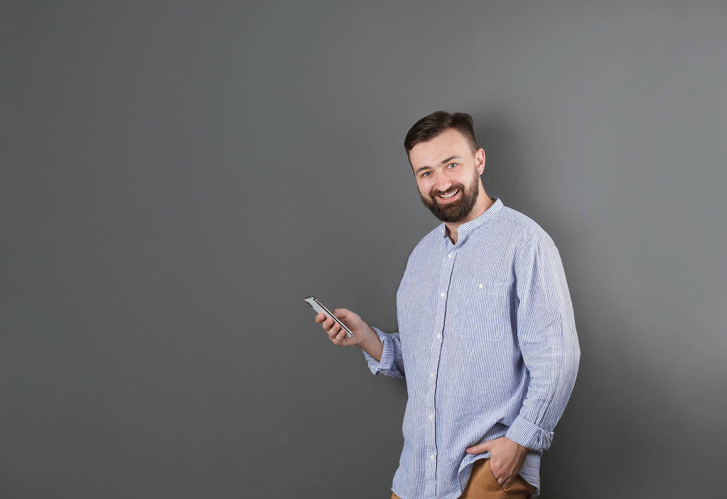 Πορτρέτο του όμορφος γενειοφόρος άνδρας με το κινητό στο χρώμα φόντου - Φωτογραφία, εικόνα