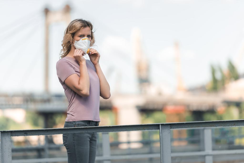 женщина носит защитную маску на мосту и смотрит в сторону, концепция загрязнения воздуха
 - Фото, изображение
