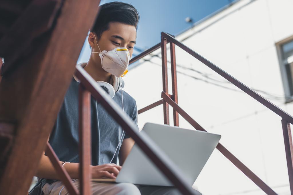 asiático adolescente en protección máscara usando laptop en escalera aire contaminación concepto
 - Foto, imagen