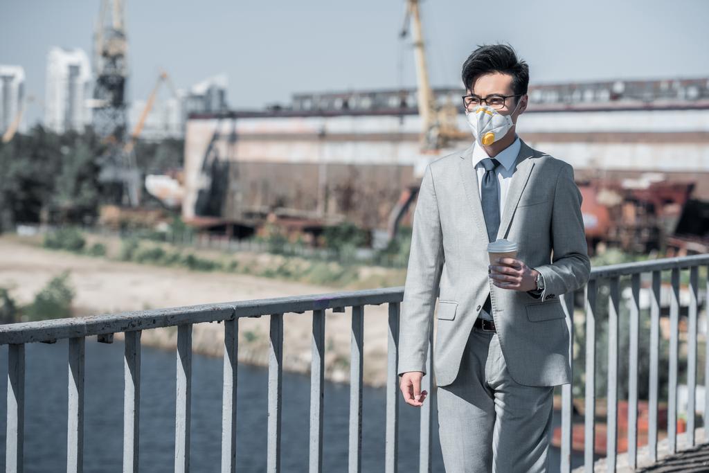 asian businessman in protective mask walking on bridge with coffee in paper cup, air pollution concept - Photo, Image
