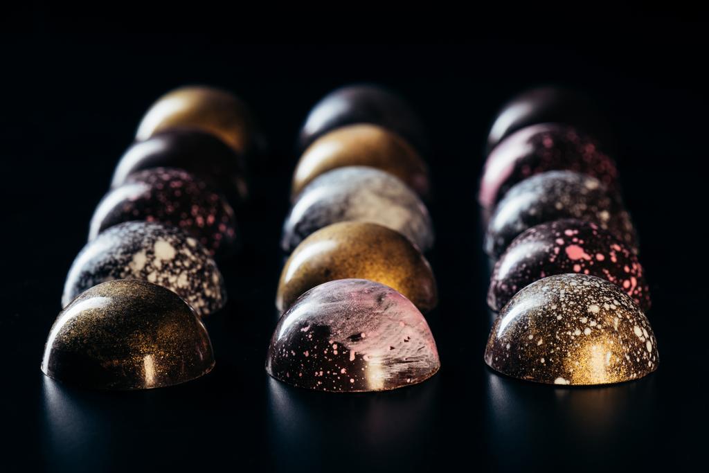 lähikuva suklaamakeisista, jotka on sijoitettu riveihin mustalla taustalla
  - Valokuva, kuva