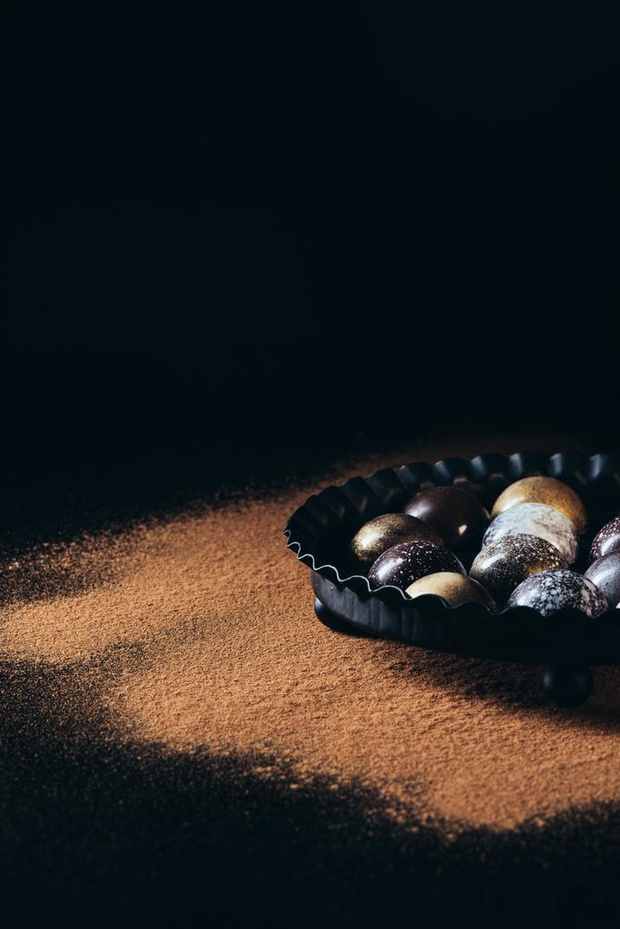 κλείνω πάνω θέα του σωρό διαφορετικές καραμέλες από σοκολάτα σε μπολ σε μαύρο φόντο - Φωτογραφία, εικόνα