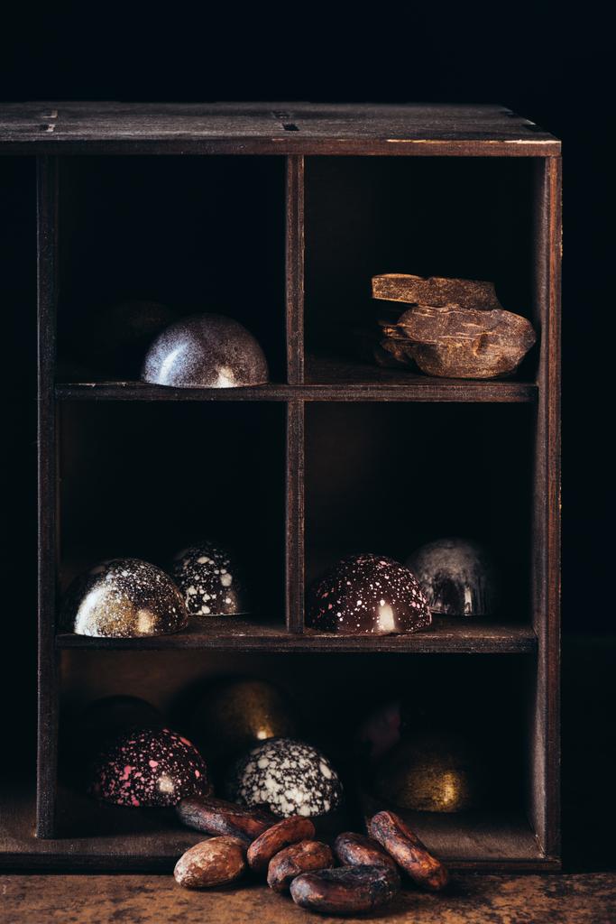 Крупный план орехов, кусочков шоколада и конфет на полках на черном фоне
 - Фото, изображение