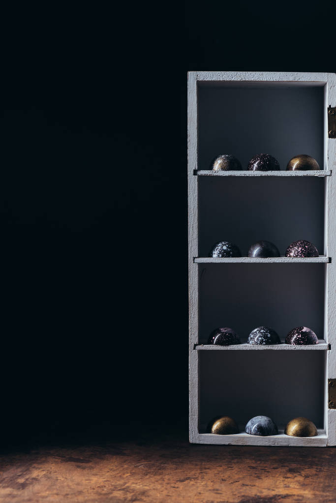diferentes caramelos de chocolate colocados en filas en estantes sobre fondo negro
 - Foto, Imagen