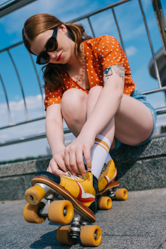 low angle view of stylish girl in sunglasses wearing roller skates on street - Photo, Image