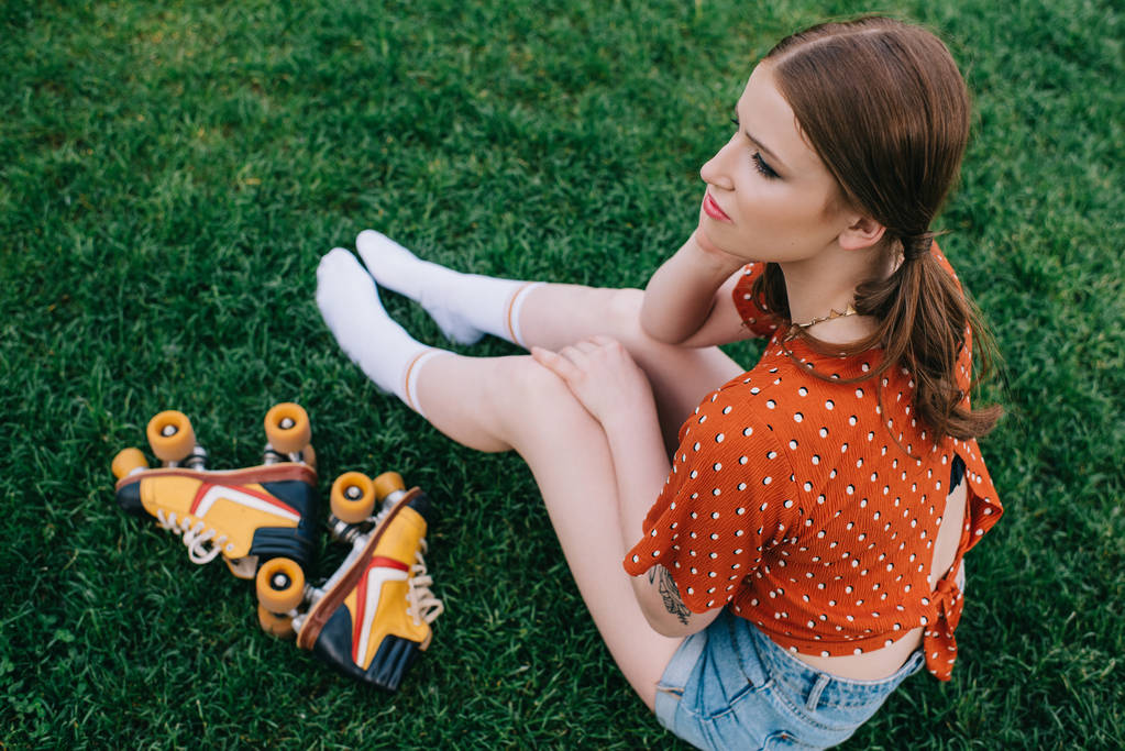 wysoki kąt widzenia dziewczyna z rolki rolki siedząc na trawie i szukasz drogi - Zdjęcie, obraz
