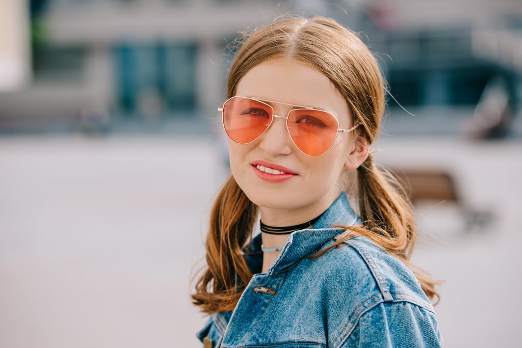portrait of beautiful young woman in sunglasses and denim jacket smiling at camera - Photo, Image