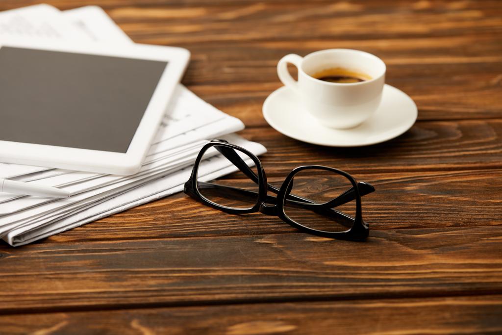 φλιτζάνι καφέ γυαλιά, ψηφιακό tablet και σωρό των εφημερίδων στο φόντο ξύλινη  - Φωτογραφία, εικόνα