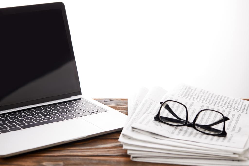 lunettes sur les journaux et ordinateur portable avec écran blanc sur la surface en bois, sur blanc
 - Photo, image