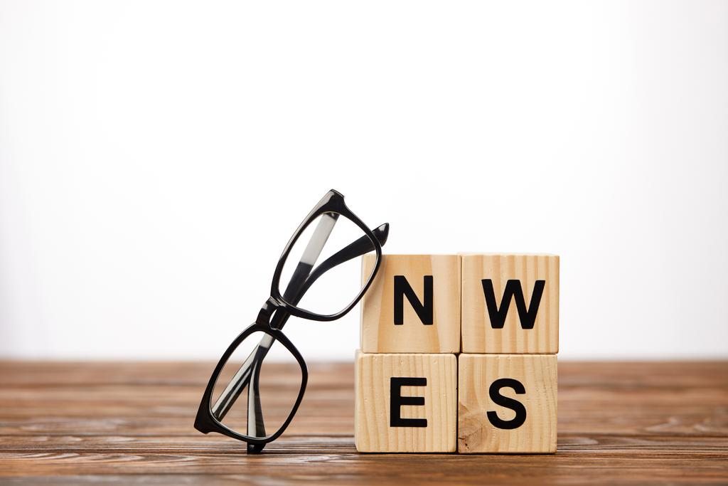 óculos e cubos alfabeto fazendo notícias palavra na superfície de madeira, no fundo branco
 - Foto, Imagem