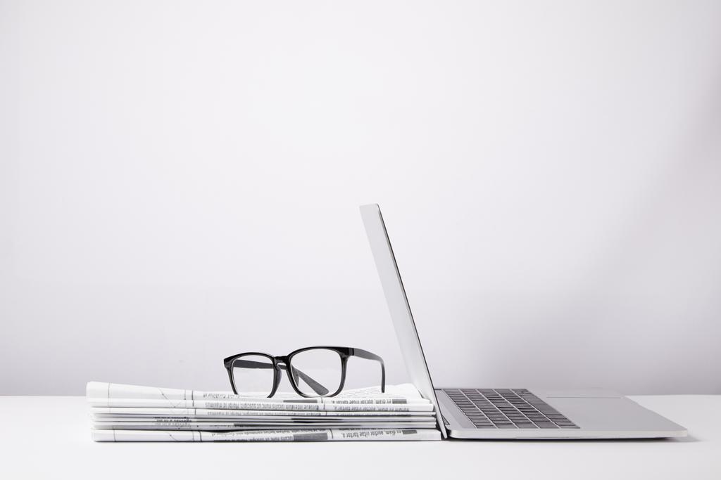 laptop e óculos em montão de jornais, em branco
 - Foto, Imagem