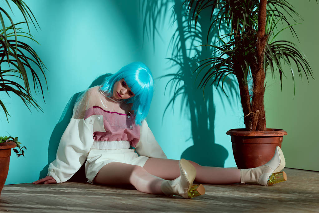 stylová holka v modrá paruka předstírá panenku a sedí na podlaze mezi hrnkové rostliny  - Fotografie, Obrázek