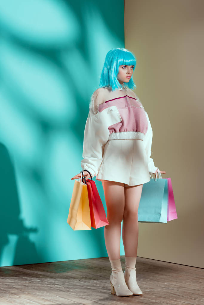 volle lengte weergave van modieuze jonge vrouwelijke model in blauwe pruik boodschappentassen te houden en weg op zoek - Foto, afbeelding