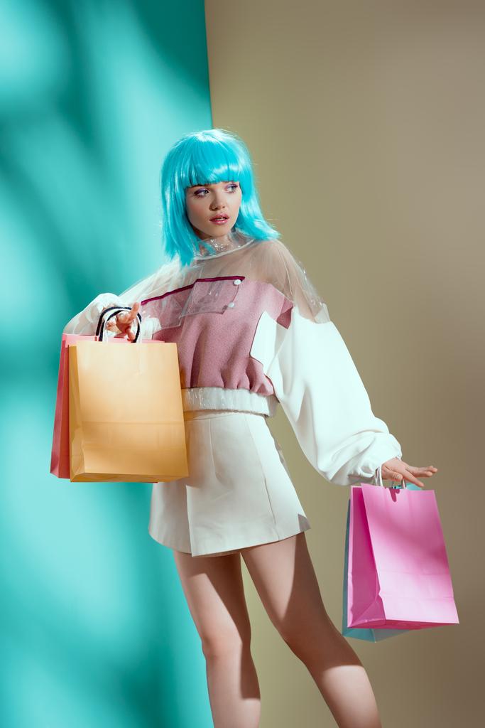 attractive stylish girl in blue wig holding paper bags and looking away in studio  - Photo, Image