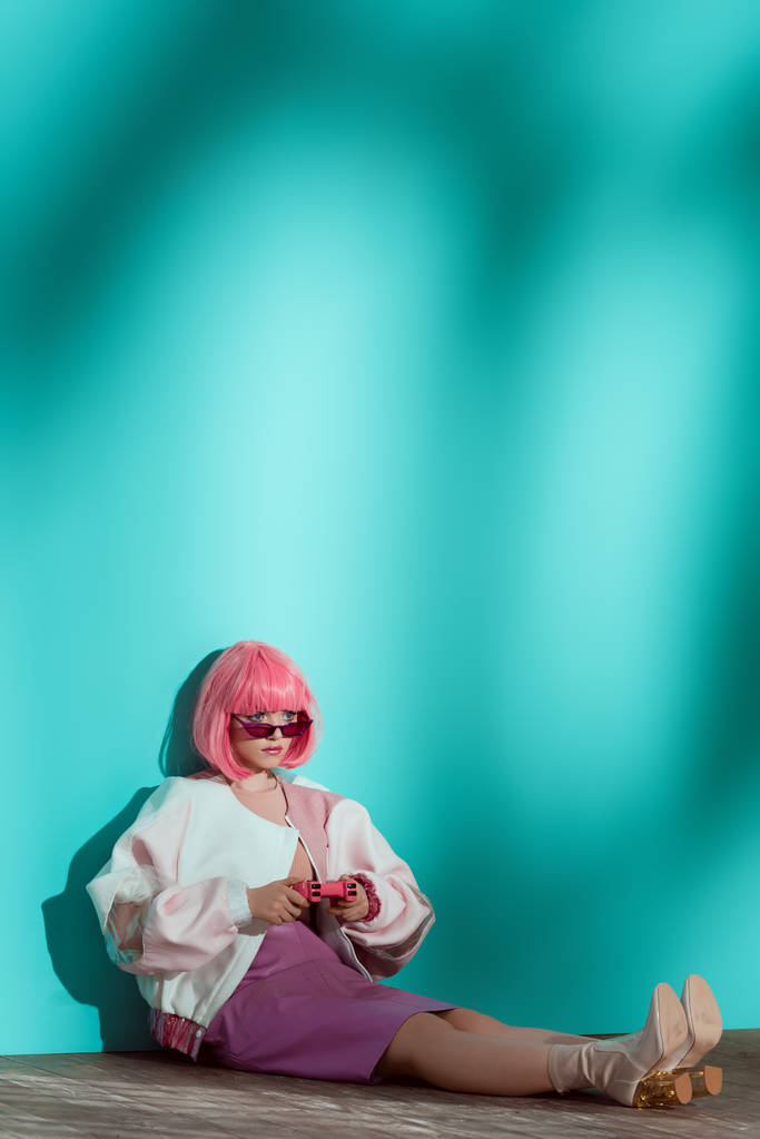 vue pleine longueur de jeune modèle féminin à la mode en perruque lumineuse jouant avec une manette rose
 - Photo, image