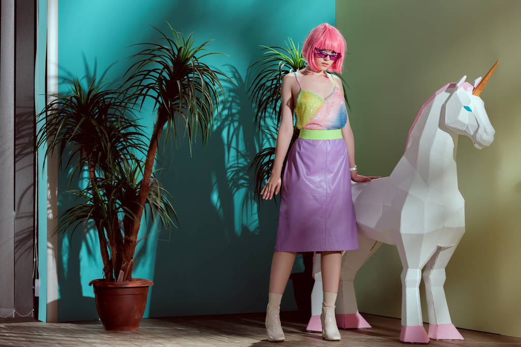 ελκυστικό κομψό κορίτσι στο ροζ περούκα στέκεται κοντά μονόκερος και βλέπουν τα φωτογραφικών μηχανών - Φωτογραφία, εικόνα