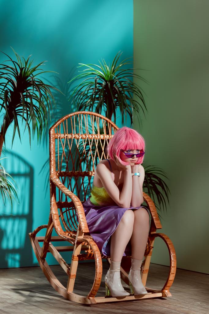 красивая стильная скучающая девушка в розовом парике сидит в кресле-качалке и смотрит в сторону
 - Фото, изображение