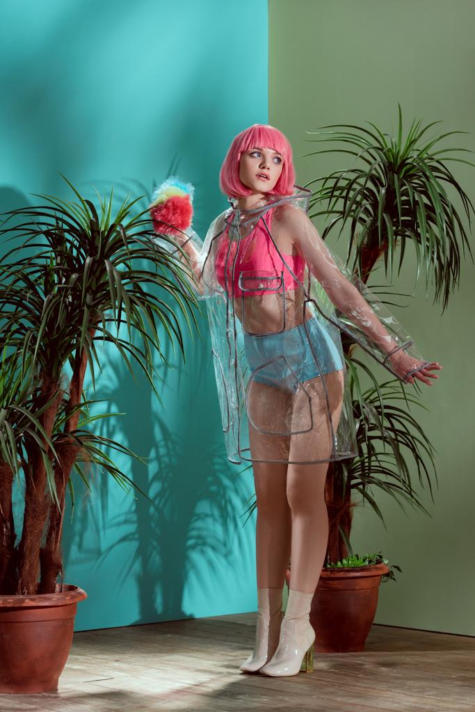 dívka v růžové paruce a transparentní pláštěnka předstírá panenku a hledat dál ve studiu - Fotografie, Obrázek