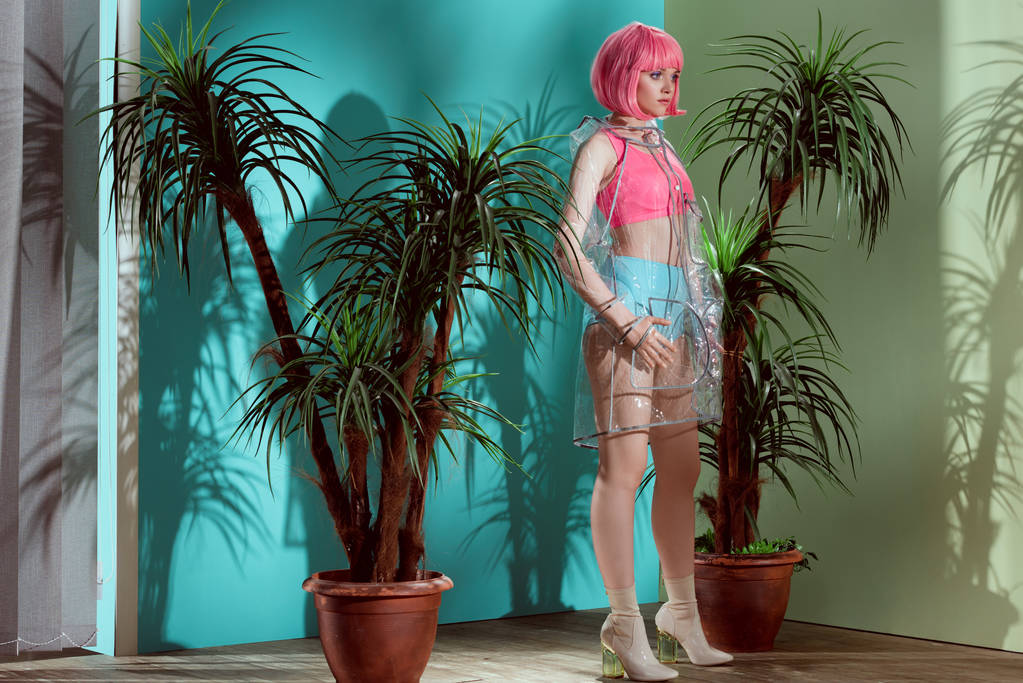 gyönyörű női modell, a rózsaszín paróka és átlátható esőkabát pózol stúdió  - Fotó, kép
