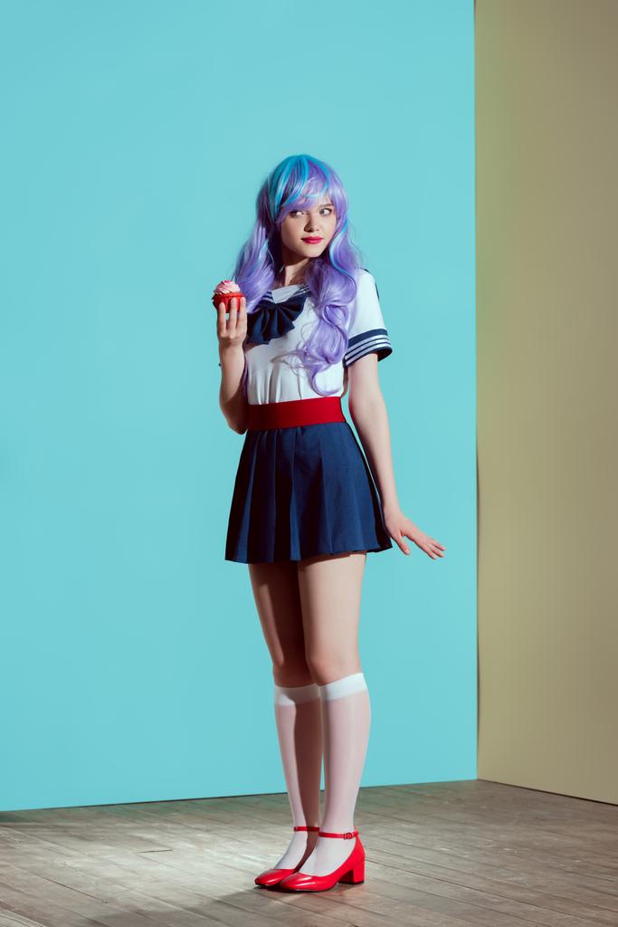 full length view of beautiful girl in bright wig holding sweet cupcake in studio - Photo, Image