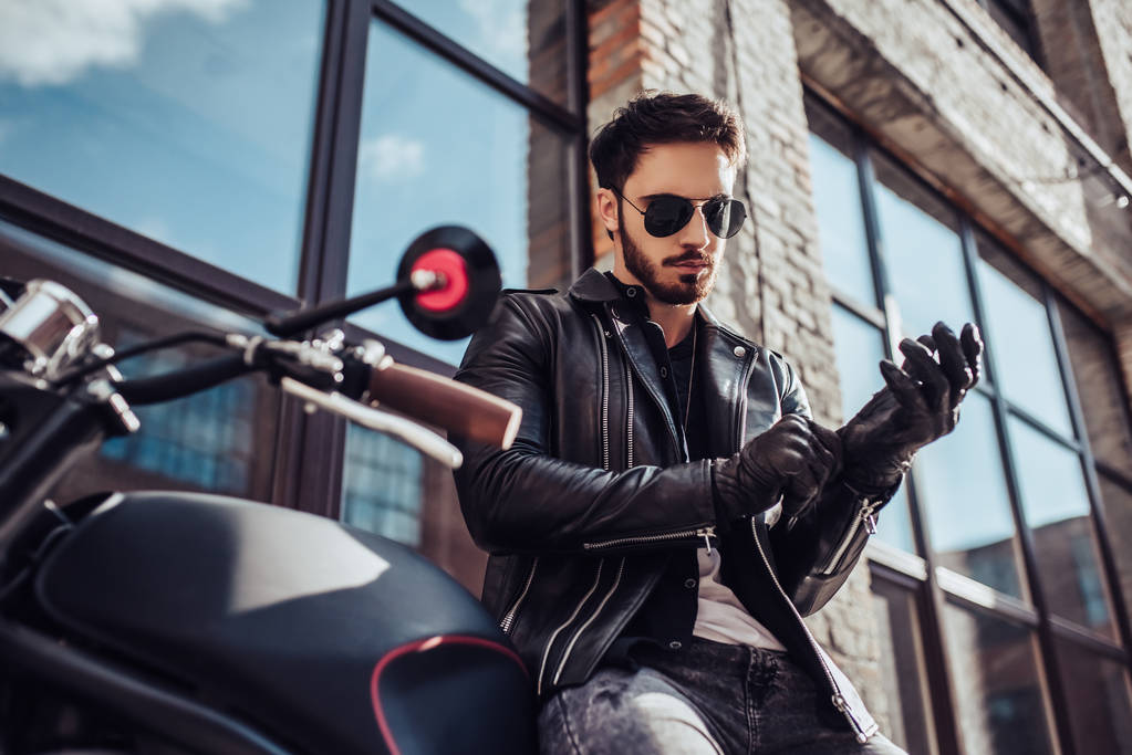 オートバイの古典的なスタイルを黒でハンサムなひげを生やしたバイクに乗る人。カフェ レーサー. - 写真・画像