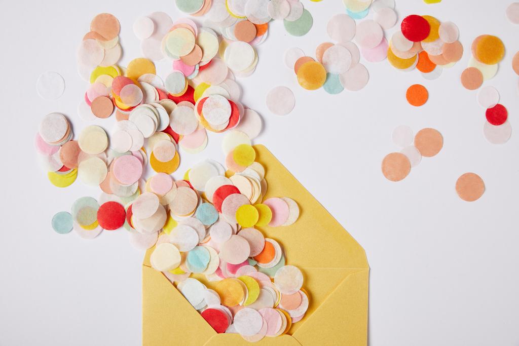 vue de dessus des morceaux de confettis colorés et enveloppe jaune sur la surface blanche
 - Photo, image