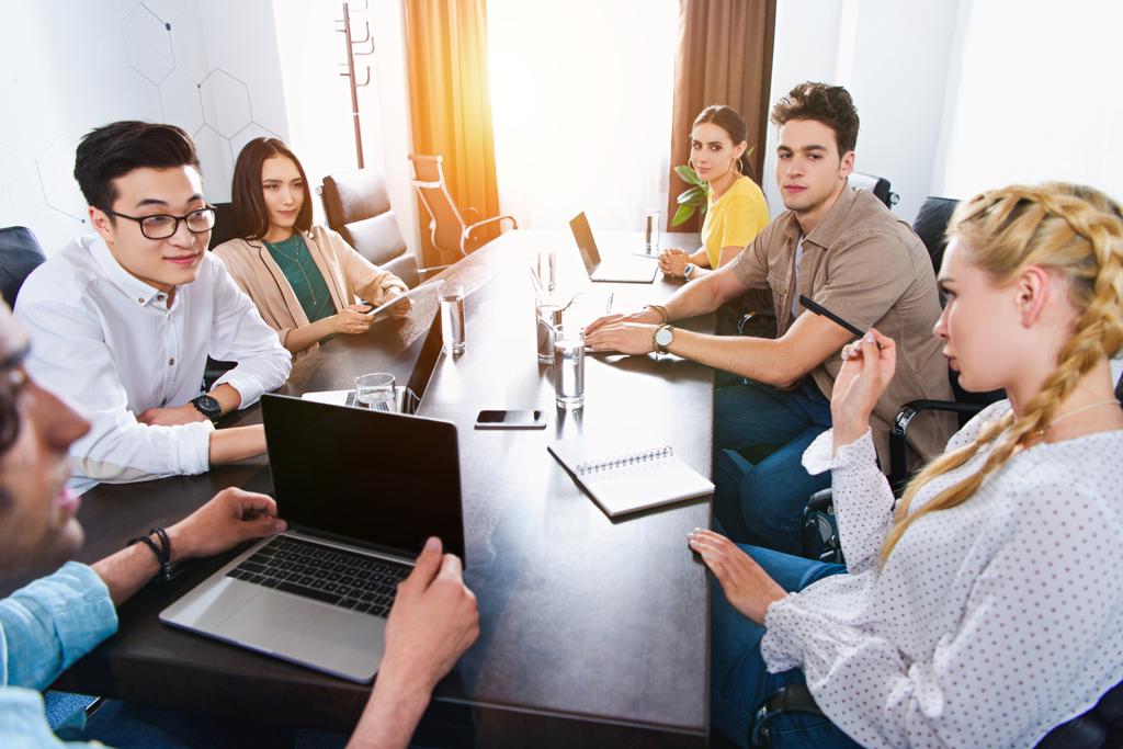 image recadrée de partenaires d'affaires multiculturels se réunissant à table avec des ordinateurs portables dans un bureau moderne
  - Photo, image