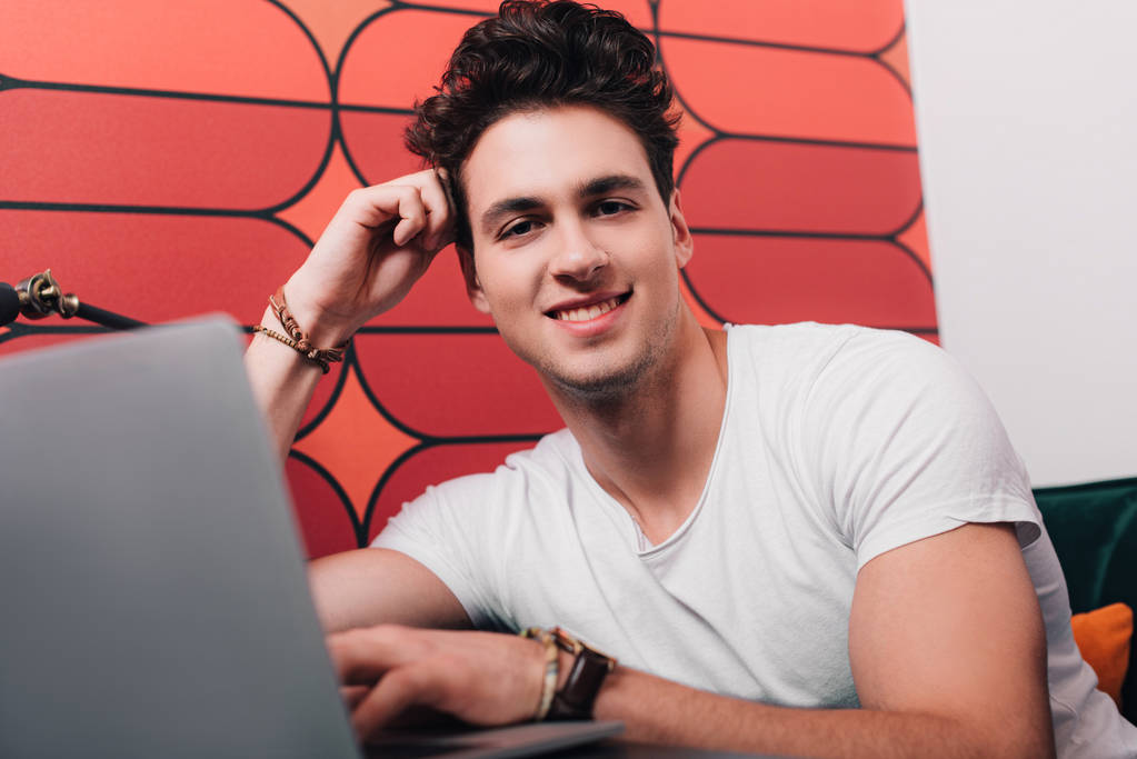 χαμογελαστός νεαρός επιχειρηματίας που εργάζεται στο lap-top στο σύγχρονο γραφείο  - Φωτογραφία, εικόνα