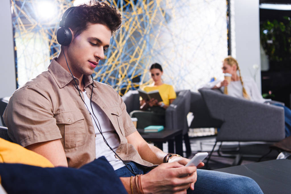 νεαρός επιχειρηματίας στα ακουστικά χρησιμοποιώντας το smartphone στο σύγχρονο coworking γραφείο  - Φωτογραφία, εικόνα