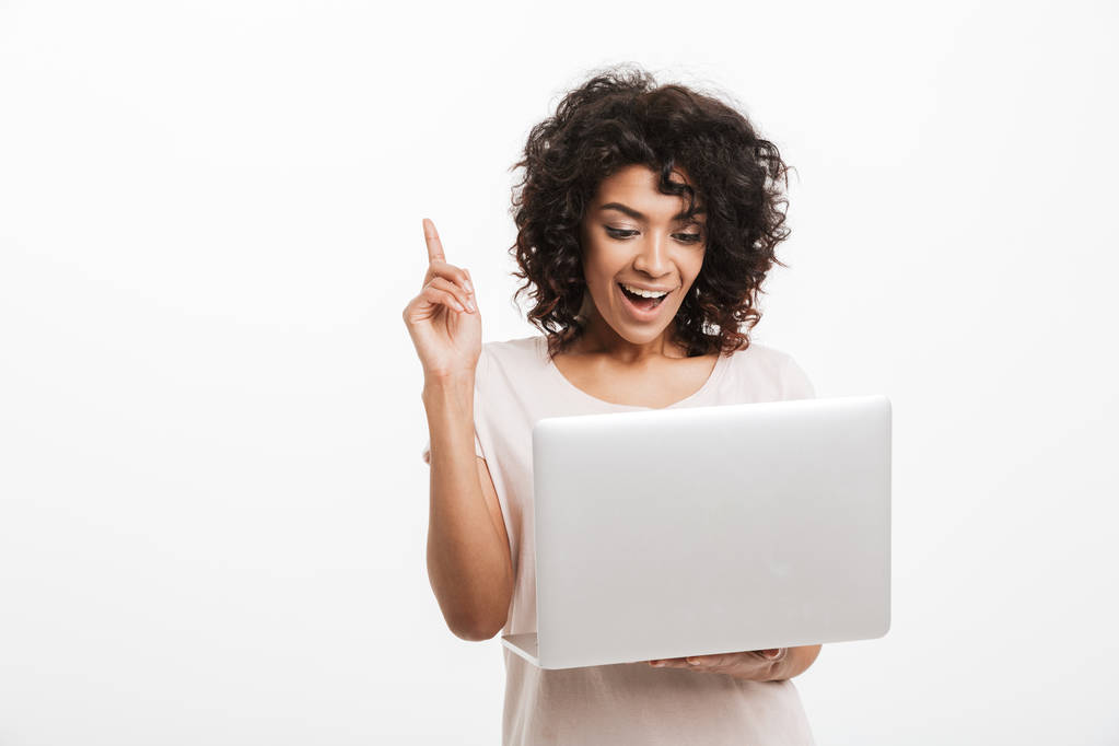 Boldog fiatal afro-amerikai nő gazdaság laptop számítógép, és ujját felfelé mutató elszigetelt fehér háttér felett portréja - Fotó, kép
