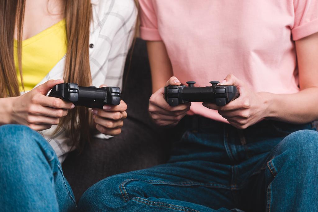 imagem cortada de duas amigas com joysticks nas mãos jogando videogame
  - Foto, Imagem
