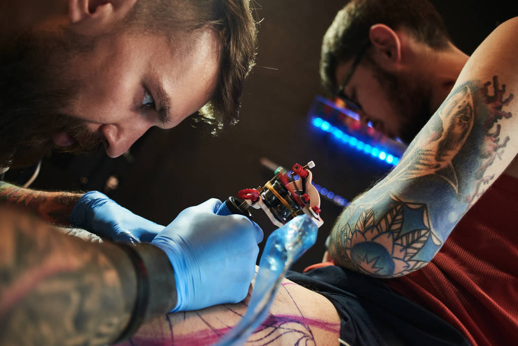 koncentrovaný muž tetování mistr tetování na noze klienta podle tetování stroj, detail - Fotografie, Obrázek