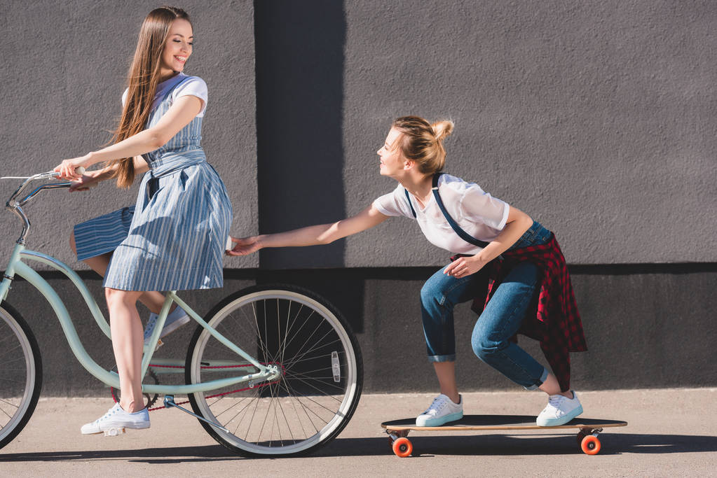 femme souriante à vélo et remorquant son amie sur skateboard
  - Photo, image