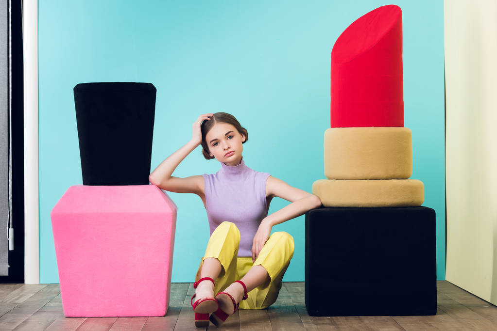 attraktives Teenie-Mädchen sitzt zwischen großem Nagellack und Lippenstift  - Foto, Bild