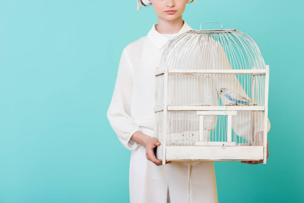 Обрезанный вид девочки в белой клетке с попугаем, изолированной на бирюзе
 - Фото, изображение