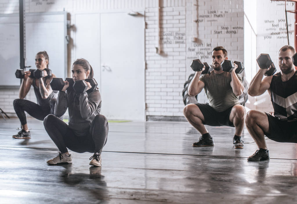 Groep van sporters doen squats met gewichten op sportschool. - Foto, afbeelding