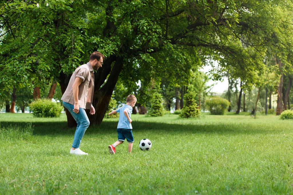 puolella näkymä isä ja poika pelaa jalkapalloa puistossa
 - Valokuva, kuva