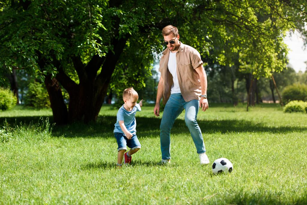 vader en zoon voetballen op het gras in het park - Foto, afbeelding