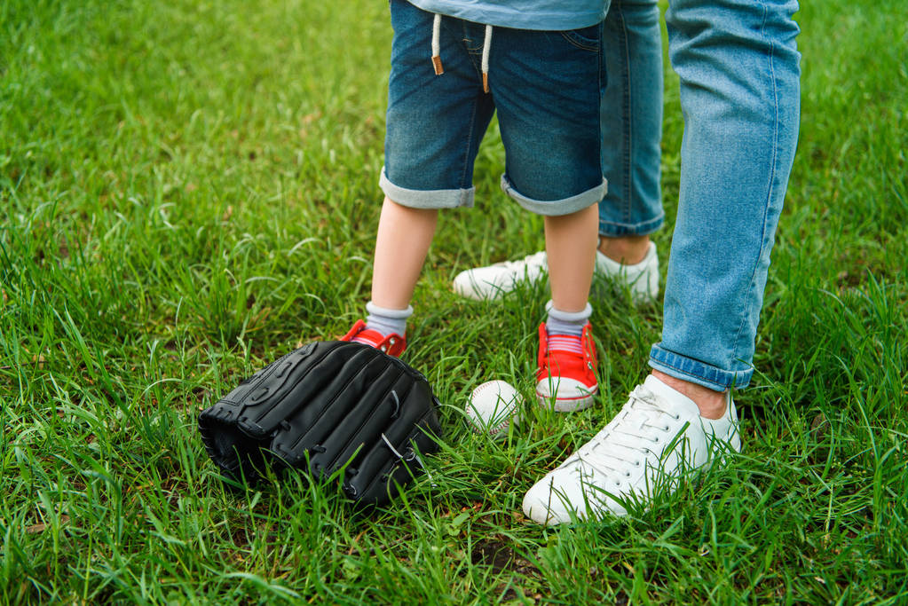 körülvágott kép az apa és fia állva fű közelében baseball labda és kesztyű - Fotó, kép