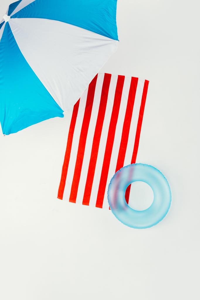 вид сверху на пляжный зонтик, полосатое полотенце и надувное кольцо, изолированное на белом
 - Фото, изображение