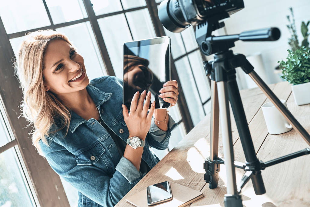 Jovem blogueira mulher em uso casual mostrando tablet digital e sorrindo durante a gravação de vídeo
 - Foto, Imagem