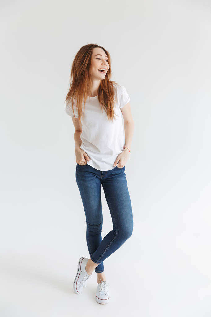 Imagen completa de Mujer alegre en camiseta posando con los brazos en los bolsillos y mirando hacia otro lado sobre fondo gris
 - Foto, imagen