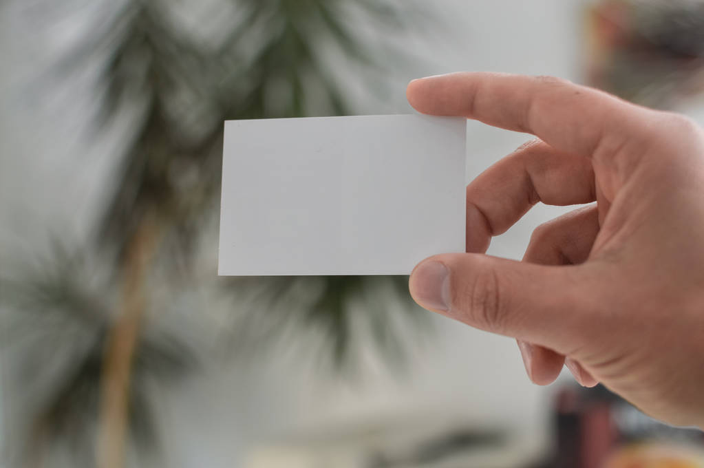 Yandan beyaz kartvizit bulanık office arka plan üzerinde gösterilen tutan bir kişinin yakın çekim - Fotoğraf, Görsel