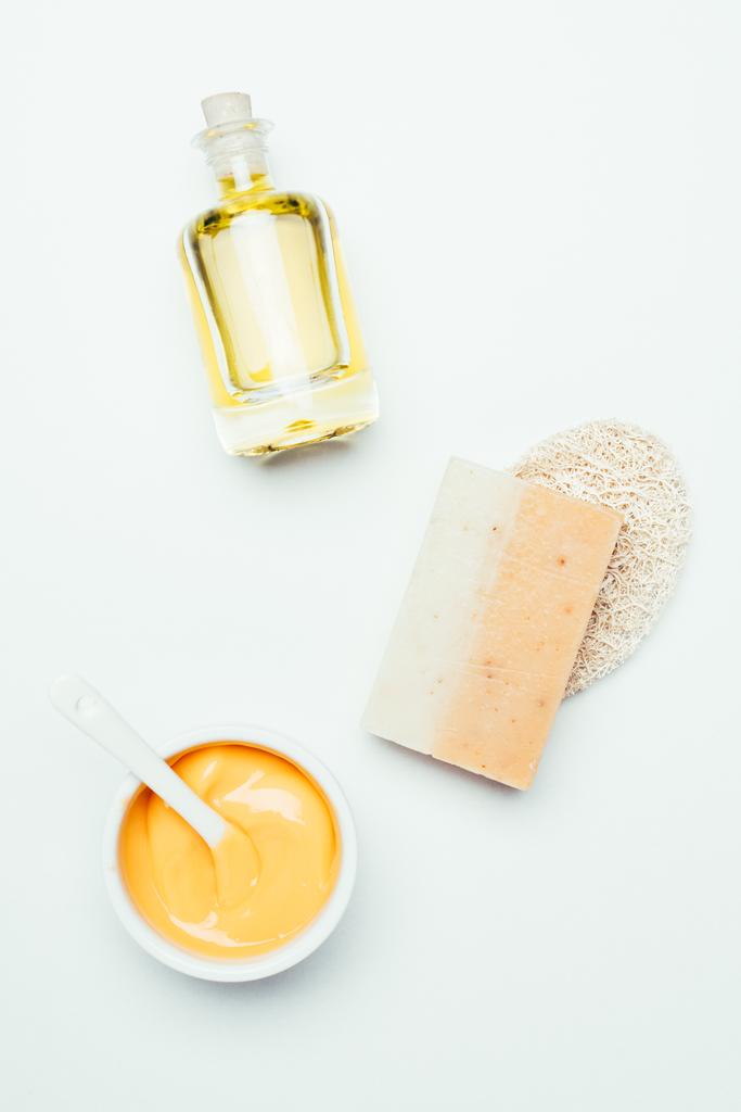 Układ płaski z gliny pomarańczowy maski w pojemniku, łyżka, gąbka, mydła i perfum butelki na białym tle na białej powierzchni - Zdjęcie, obraz